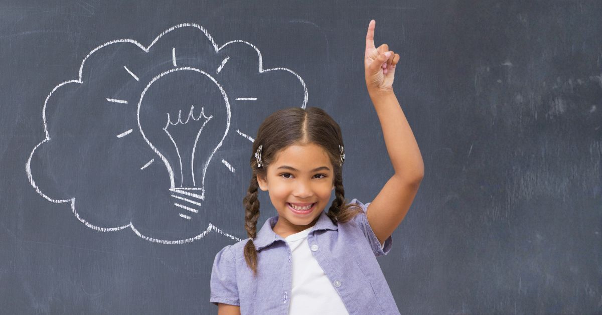 Ein Schulmädchen steht vor einer Tafel und streckt den Zeigefinger über den Kopf. Auf der Tafel ist mit weißer Kreide eine Glühbirne in einer Gedankenwolke aufgezeichnet.