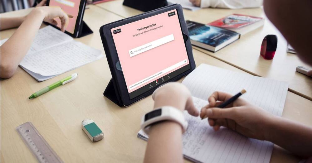 Titelbild: Tablet ist vor einer schreibenden Person aufgestellt. Der Bildschirm hat als Überschrift "Prüfungsmodus".