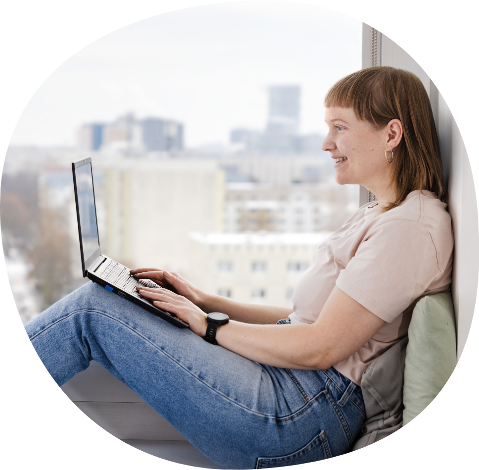 Eine junge Studentin sitzt auf einer Fensterbank und arbeitet an ihrem Laptop.