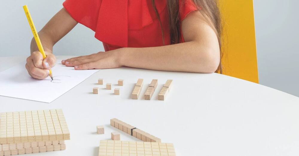 Titelbild: Mädchen schreibt Zahl auf, vor ihr liegen Therapiematerialien