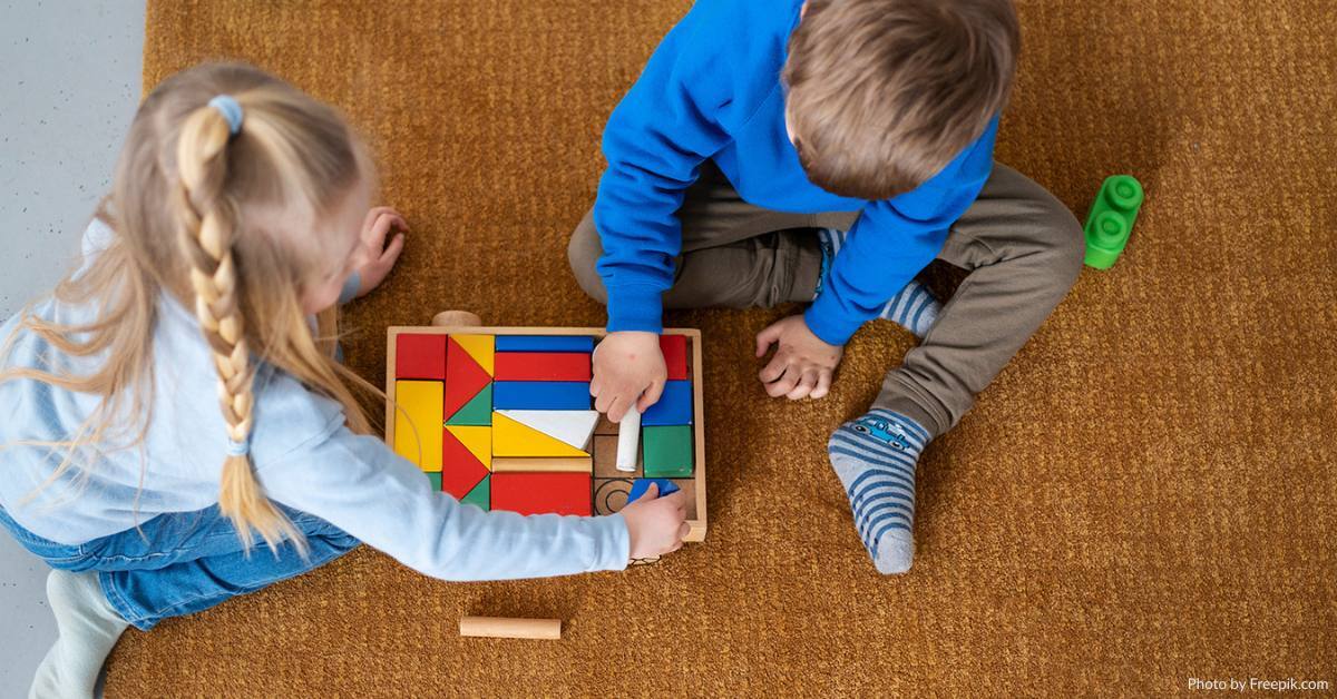 Zwei Kinder beschäftigen sich mit bunten Holzbausteinen, die in einem Holzkasten angeordnet sind.